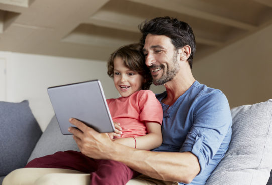 Happy father and son using digital tablet on sofa at home