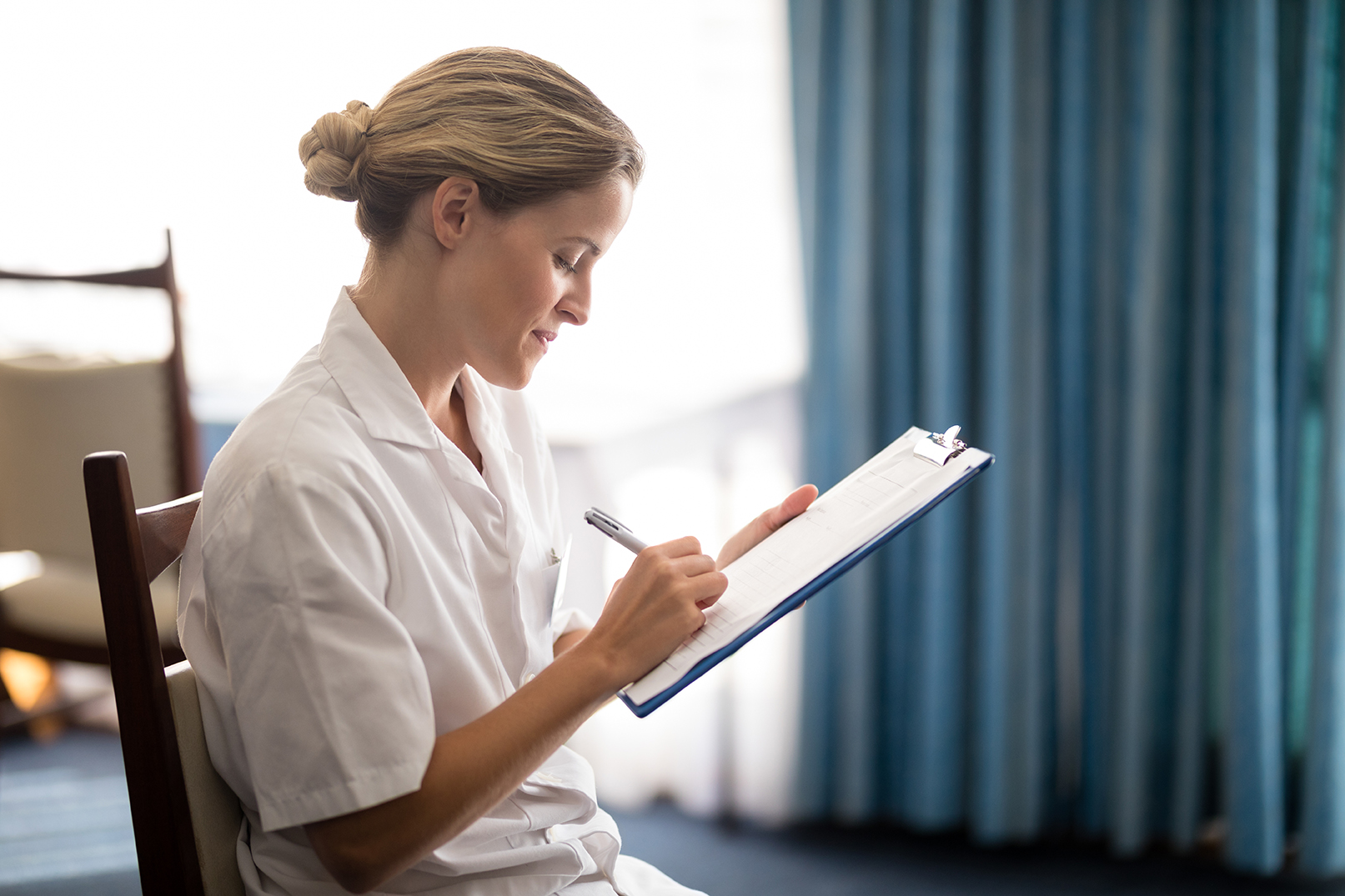 Side view of young female doctor writing on clipboard at retirement home